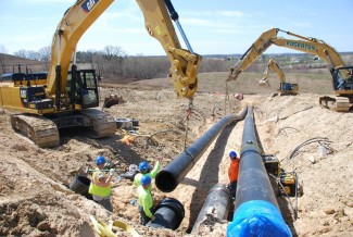 Workers use backhoes to install large pipes in a trench