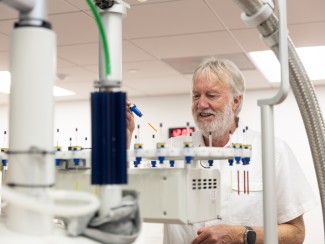 man with white hair and beard pictured behind lab equipment
