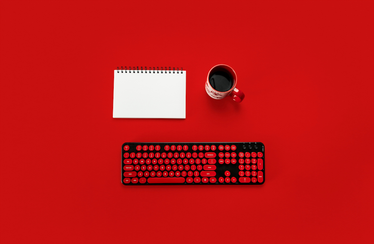 A notebook, coffee cup, and keyboard on a red background