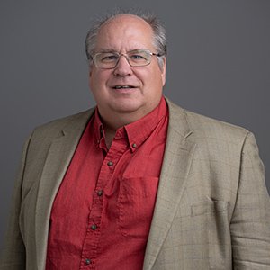 Headshot of Chris Hegna, a white man in glasses and a suit smiling.