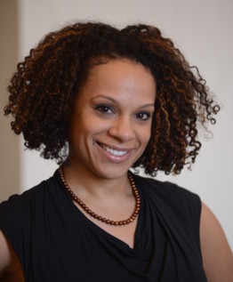 Headshot of Diana Hernandez, a feminine-presenting person with short curly brown hair, smiling and wearing a black blouse.