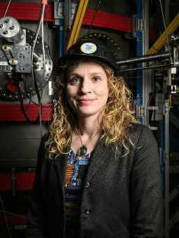 Headshot of Steffi Diem, a white woman, wearing a hard hat and smiling in front of some equipment.