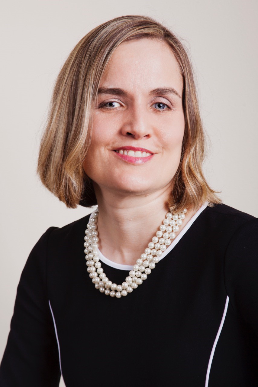 Headshot of Dr. Frederick, a feminine-presenting person smiling with shoulder-length blonde hair, wearing a black sweater and pearls.