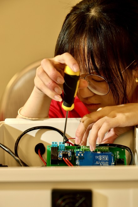 Woman with black hair and glasses peers into box while holding a screwdriver