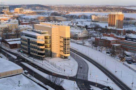 Aerial shot of wedge-shaped building at the intersection of two major streets. The building is lit by the sun while the snow-covered ground is in shadow.