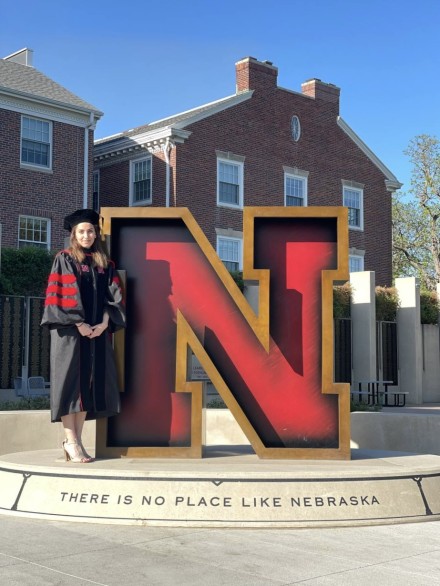 Woman in black gradation gown posing for photo next to red 'N'