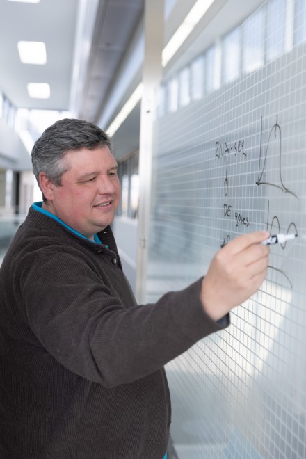 A man writes formulas on a translucent glass screen