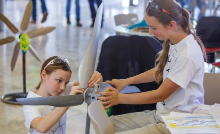 Two girls in white T-shirts work on a model wind turbine