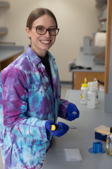 Smiling woman in tie-died lab coat and blue rubber gloves