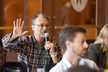 Man speaking into a microphone while holding up one hand