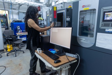woman opening the door of a refrigerator-sized machine in an electronics laboratory