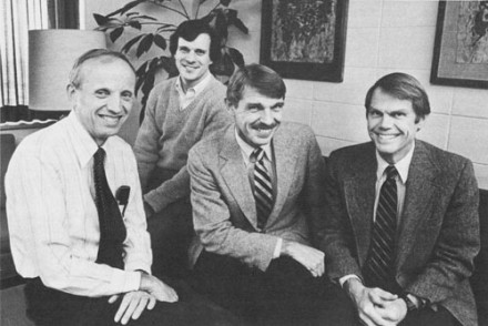 Black and white photo of four seated men smiling toward the camera