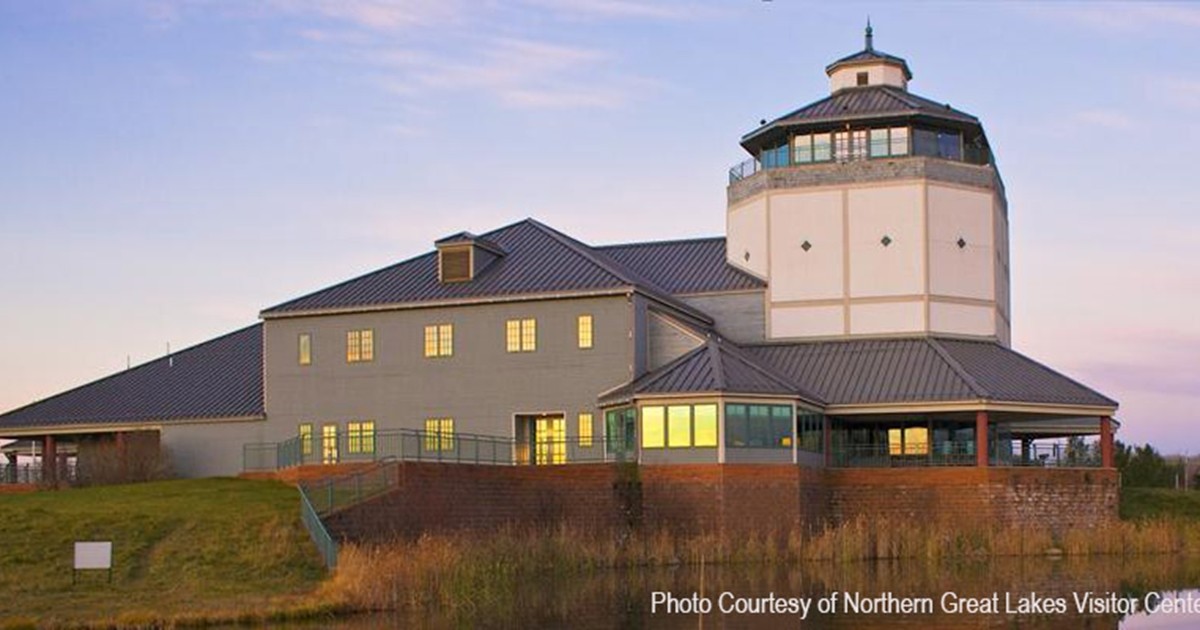 Photo of a beautiful building with yellow sunlight reflecting in the windows. A purple/blue sky arches overhead.