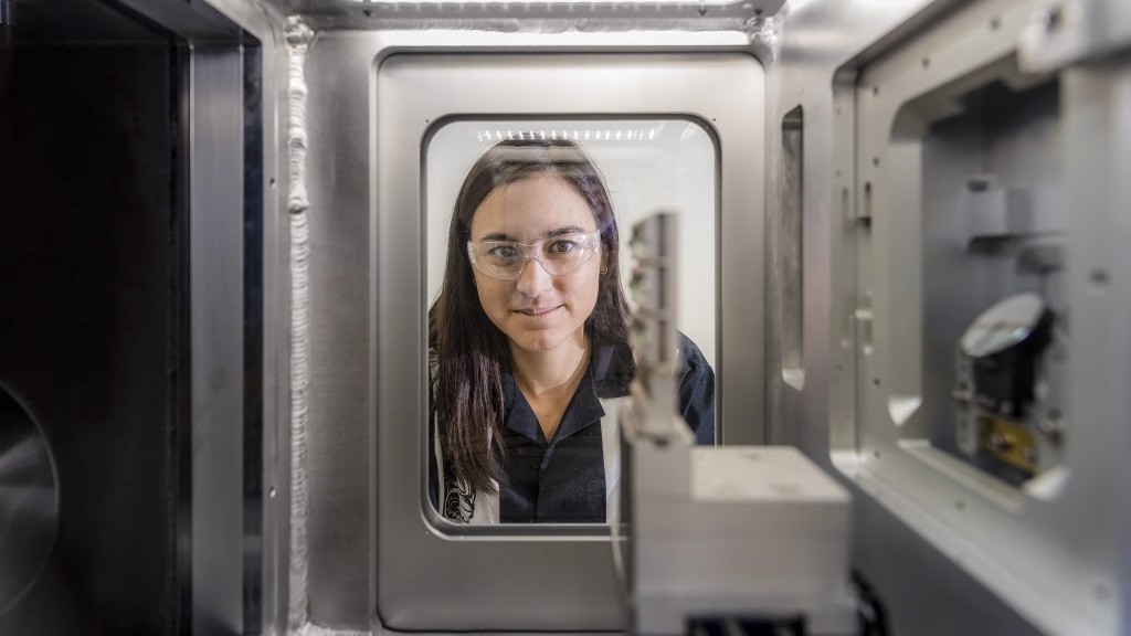 Whitney Loo peers into a piece of metal equipment through a rectangular window