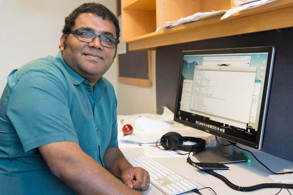 Man sitting at desk with computer monitor and keyboard turned to face camera