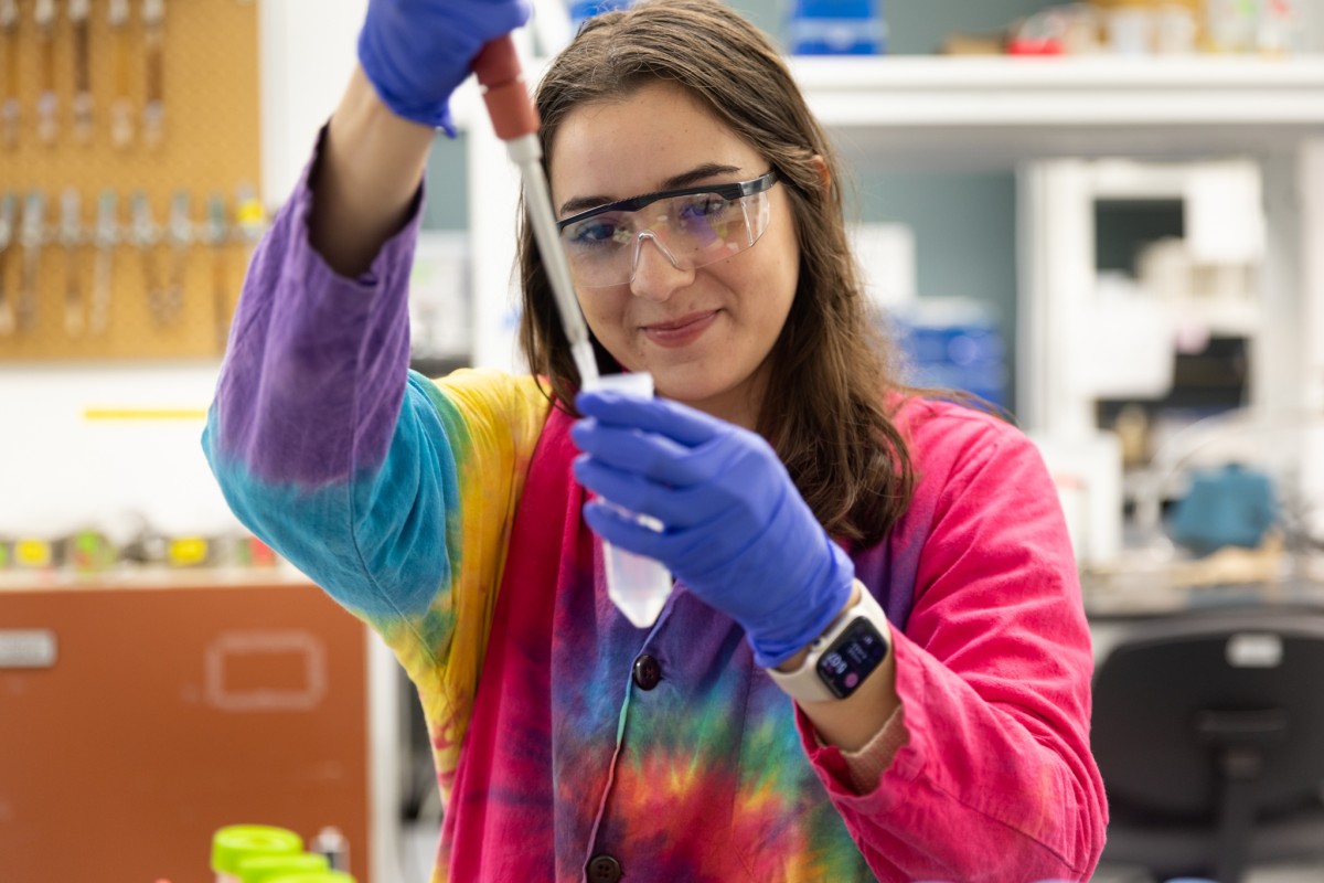 Woman with brown hair in tie-died lab coat filling test tube