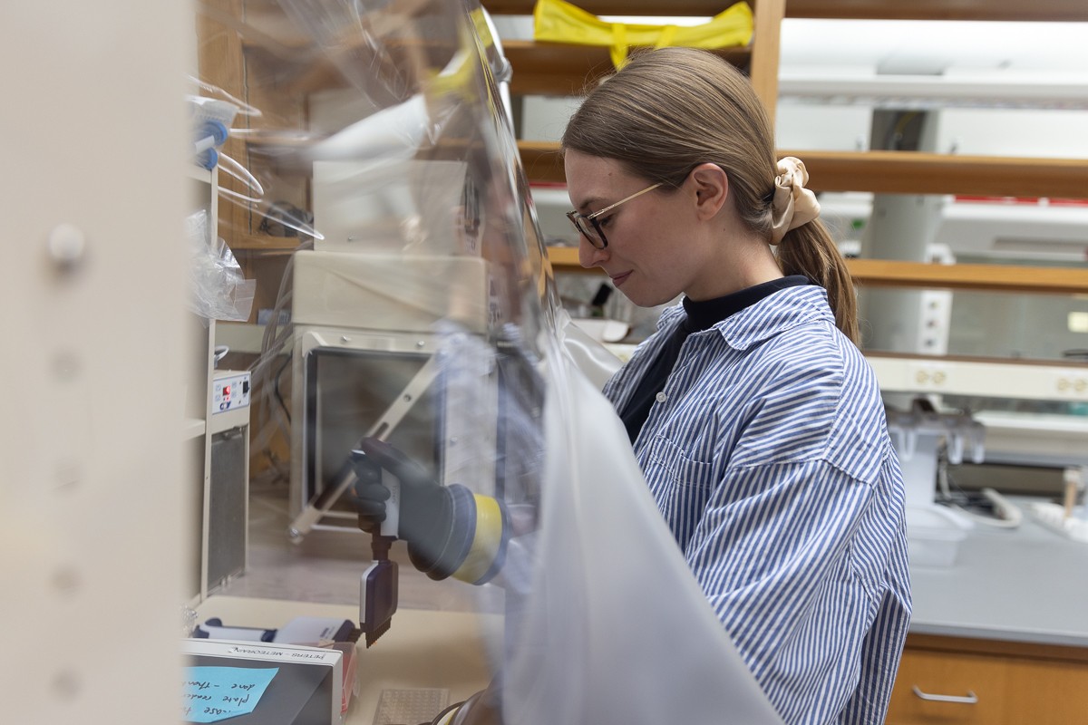 Woman with glasses and blue striped shirt works at a lab bench
