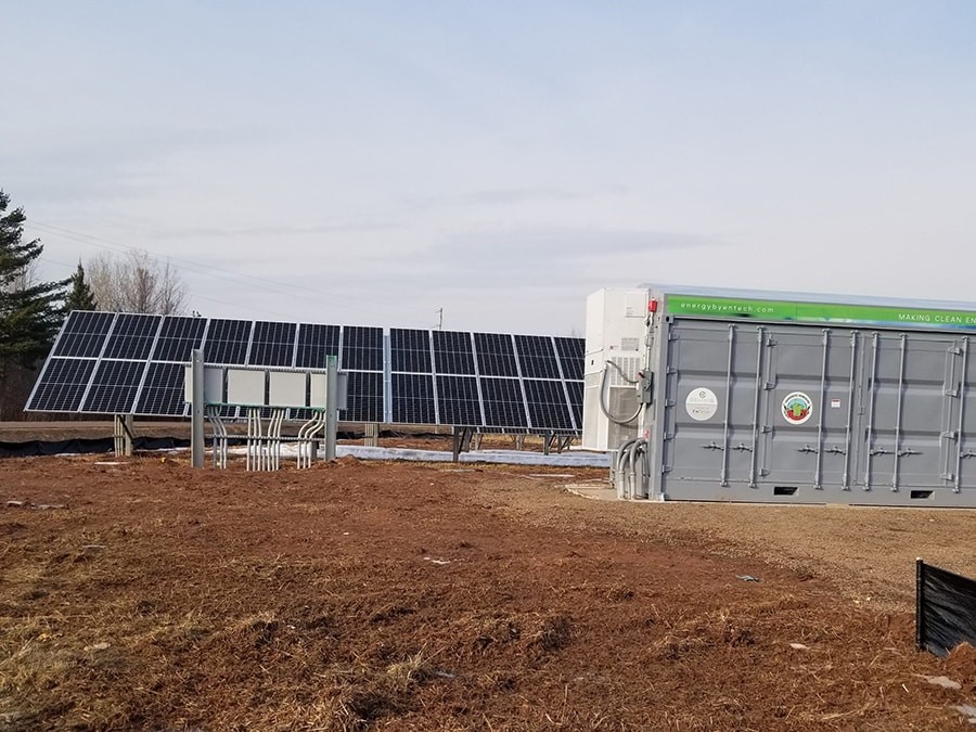An array of solar panels in the background preceded by a bank of batteries at the Bad River Wastewater Treatment site microgrid.