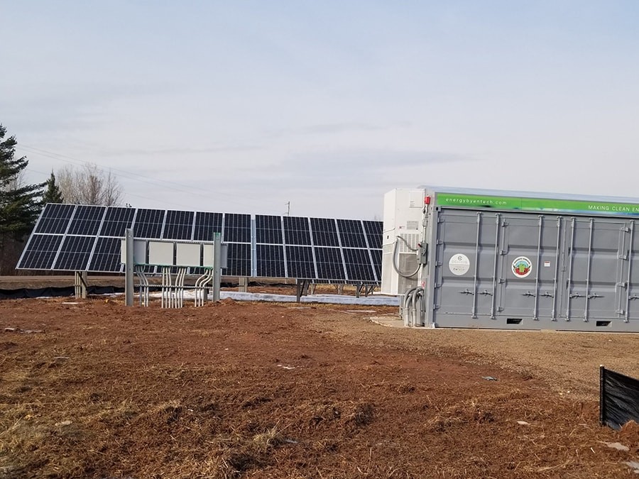 An array of solar panels in the background preceded by a bank of batteries at the Bad River Wastewater Treatment site microgrid.