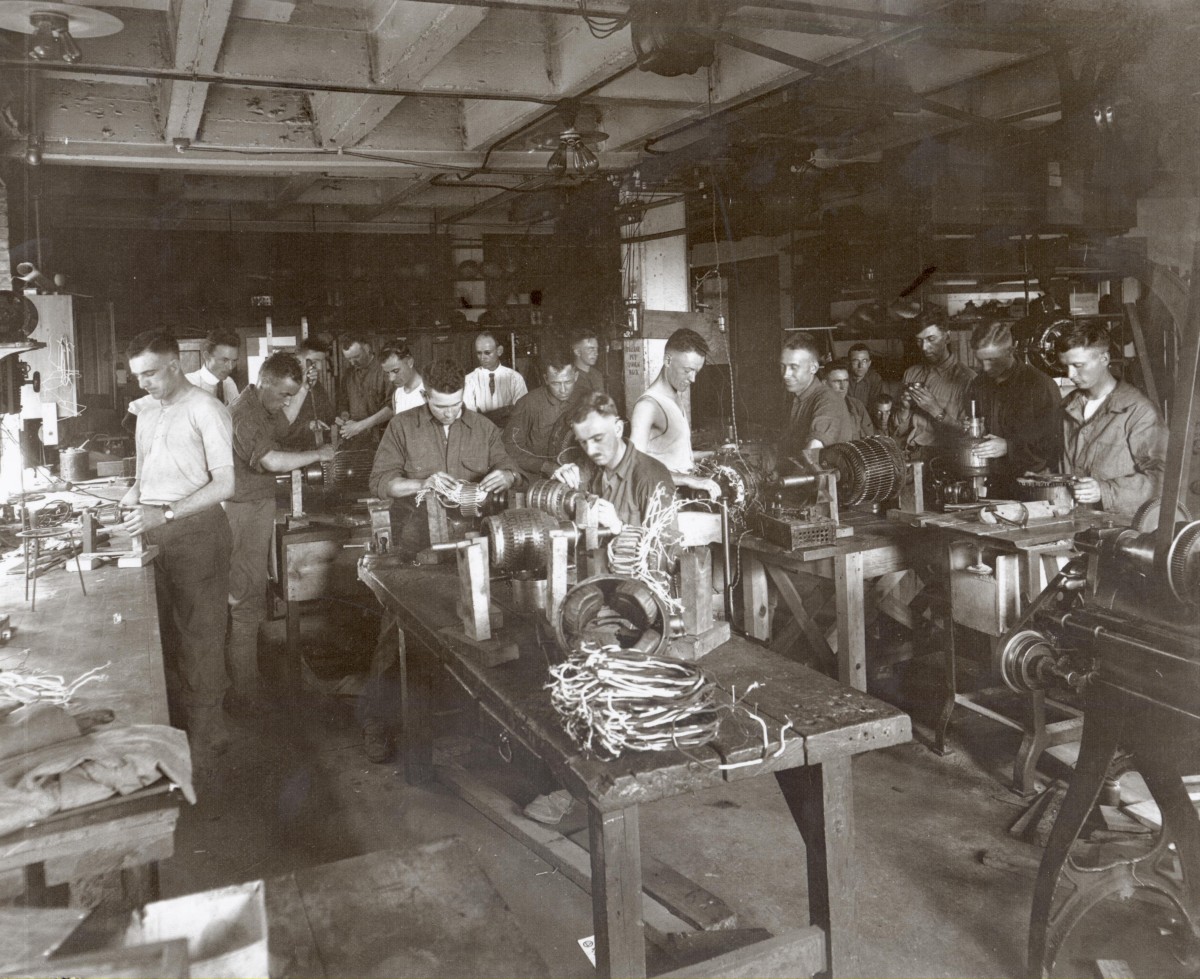 Black and white photo of young men at work in a machine shop. 