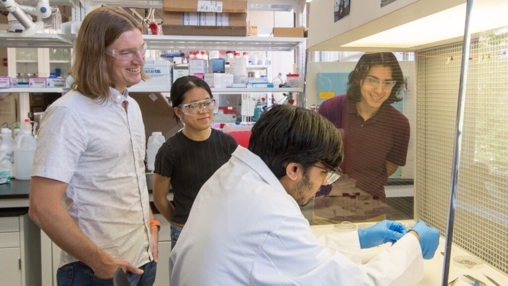 Members of Matthew Gebbie's research group stand in a circle in a lab space