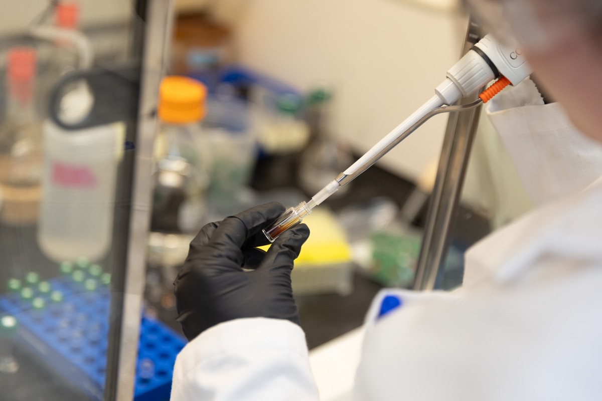 A pipette enters a small tube full of orange colored liquid