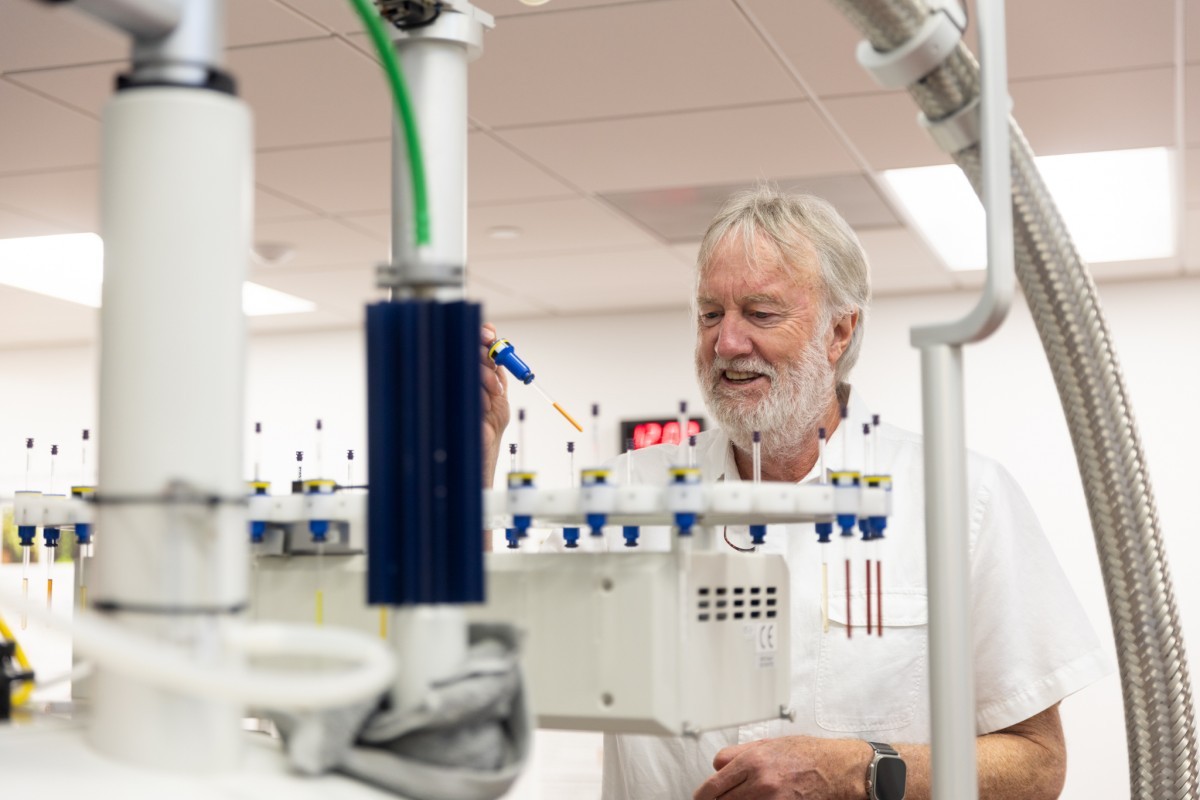 man with white hair and beard pictured behind lab equipment