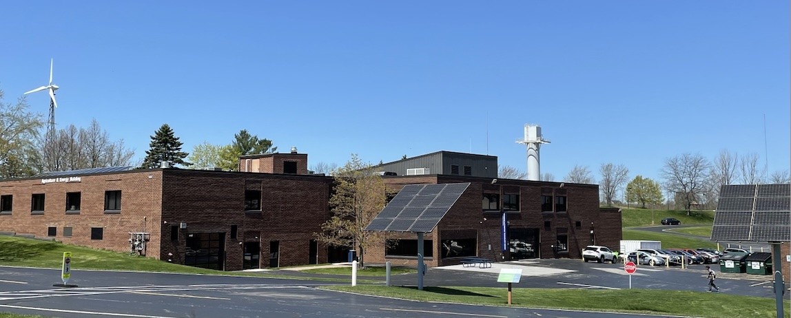 Image of a brick building with solar in front and a wind turbine in back.