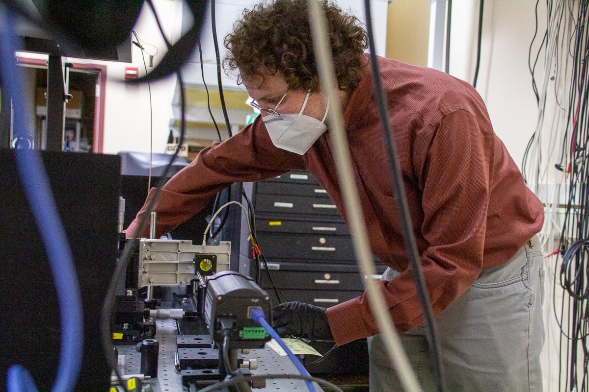 Mikhail Kats stands in front of complex instruments while making adjustments to them in his lab