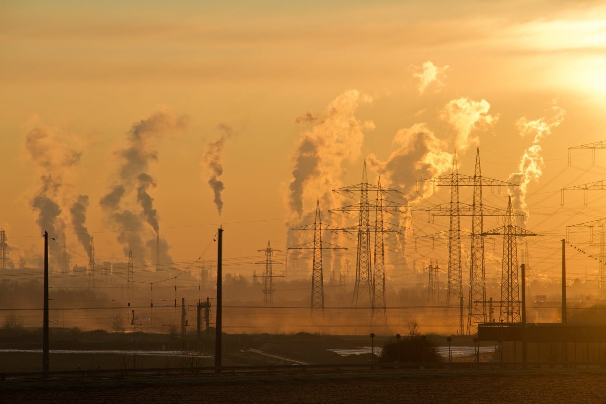 Smoke billows from stacks in front of orange sky