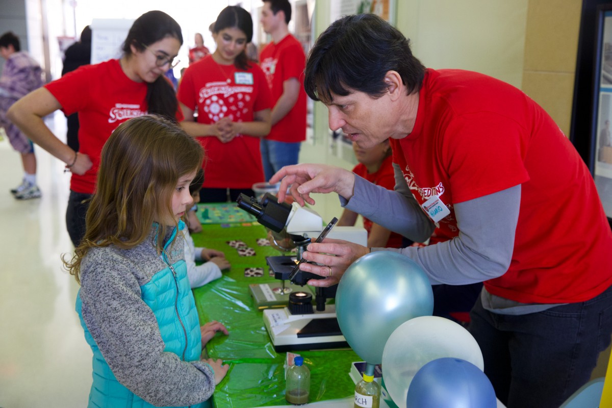 Staff scientist in red leads a young girl through an interactive activity.