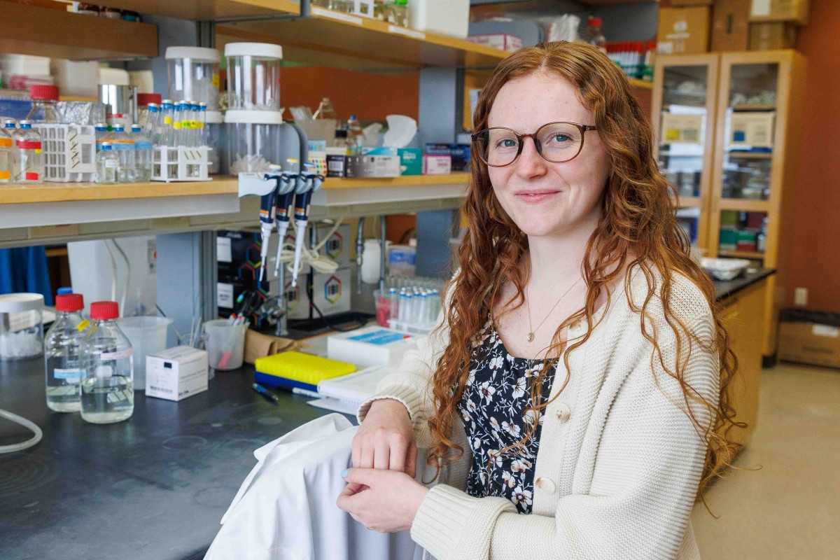Woman with red hair and glasses poses for a photo in front of a lab bench