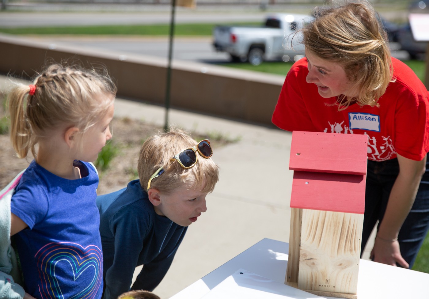 Two children look at the pollinator hotel with a scientist in a red shirt.