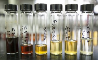 A row of six glass tubes on a lab bench containing liquids that vary in color, from dark brown on the left to clear on the right