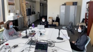 Mary Riker, left, sits at a table in front of a microphone. Michelle Chung, center, takes notes while Yiying Xiong, right answers a question on another microphone.