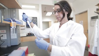 Ophelia Venturelli wearing a lab coat and pipetting at a lab bench.