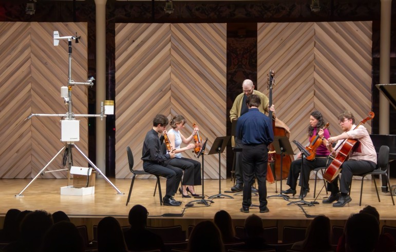 musicians on a stage next to weather monitoring equipment