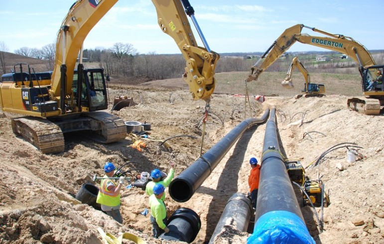 Workers use backhoes to install large pipes in a trench