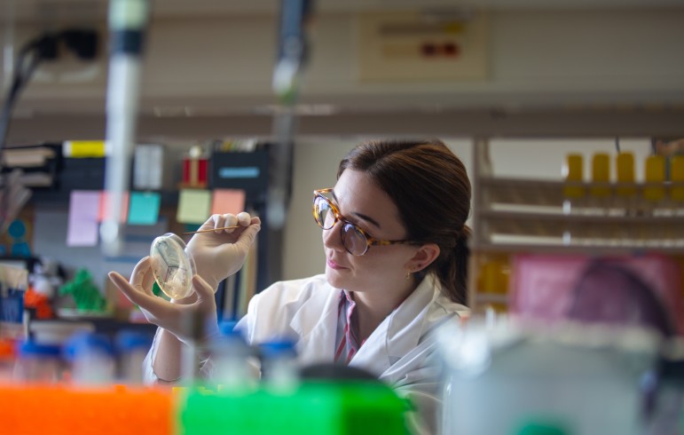 woman in lab coats examines petri dish