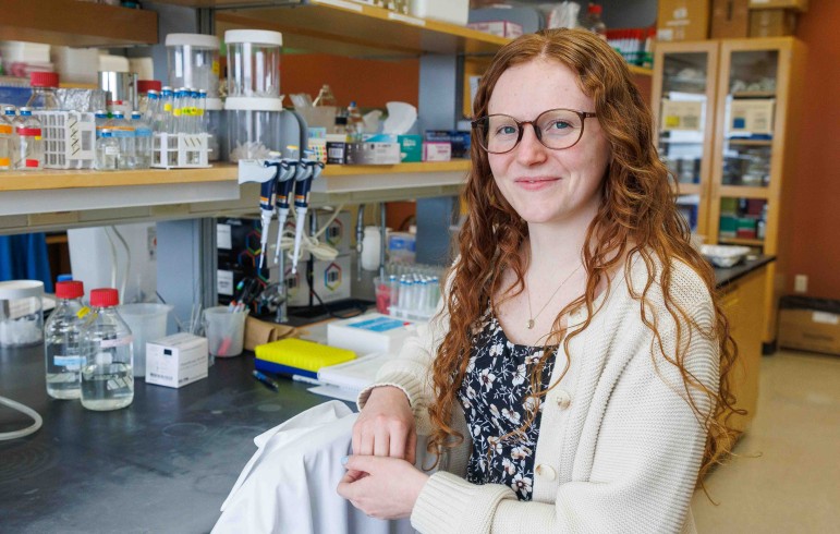 Woman with red hair and glasses poses for a photo in front of a lab bench