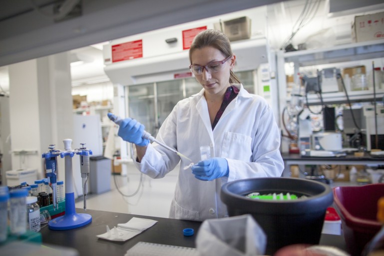 Woman in white lab coat and blue rubber gloves working at a lab bench