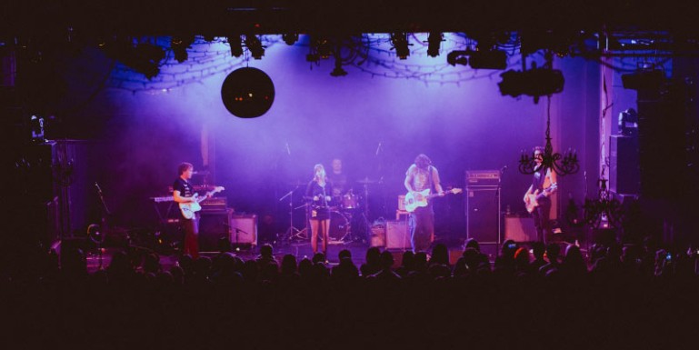 Five musicians performing on a stage in front of a purple-hued backdrop.