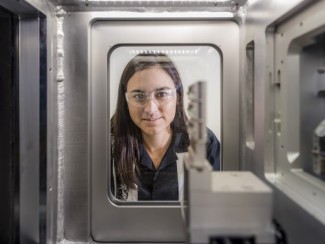 Whitney Loo peers into a piece of metal equipment through a rectangular window