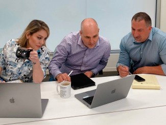 A woman and two men seated at a table look at a laptop computer screen