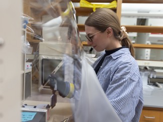 Woman with glasses and blue striped shirt works at a lab bench