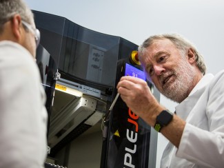 Two researchers in white lab coats examine a sample being loaded into an automated NMR or chromatography instrument (SampleJet autosampler), with a digital display showing sample number 91.