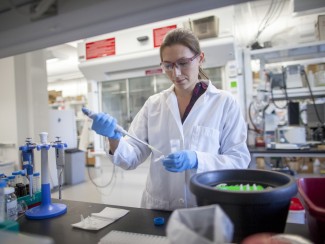 Woman in white lab coat and blue rubber gloves working at a lab bench