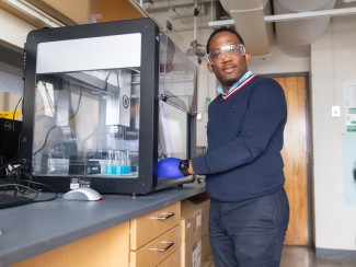 Man standing at a lab bench in front of a machine encased in metal and glass