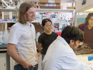 Members of Matthew Gebbie's research group stand in a circle in a lab space