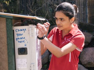 A woman stands next to the Little Free Library on State St